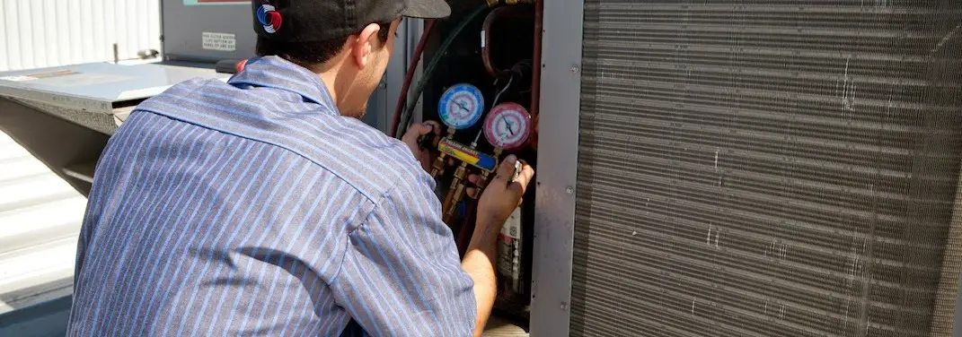 HVAC technician servicing a condenser unit in Greenfield